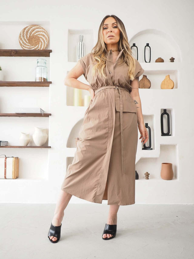 Modelo usando vestido Midi Safari Ajustável em tom bege, com fecho frontal e cintura ajustável, em ambiente moderno.