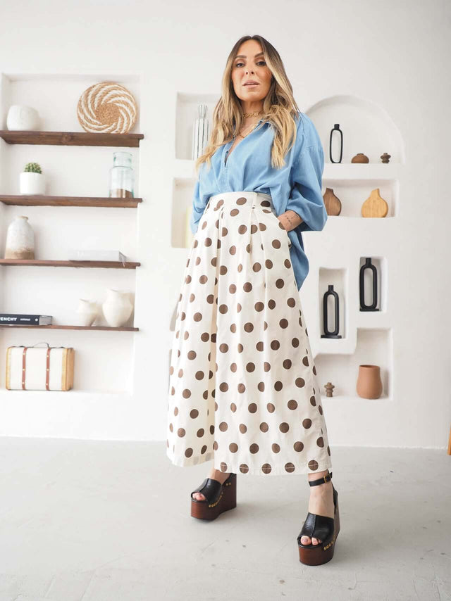 Modelo usando calças culote às bolas com blusa azul e sandálias, exibindo elegância descontraída.