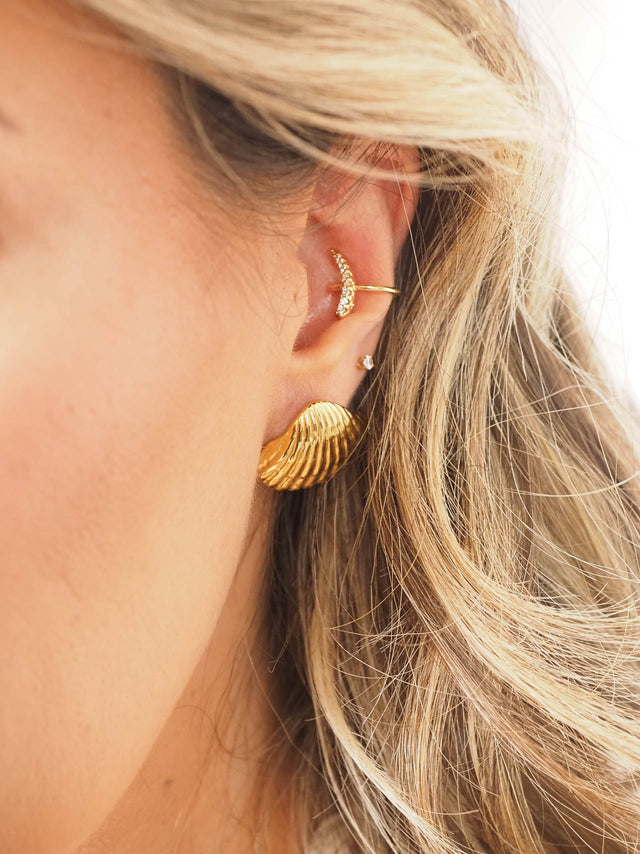 Earcuff meia lua dourado com brilhantes, destacando-se na orelha de uma mulher com cabelo solto.