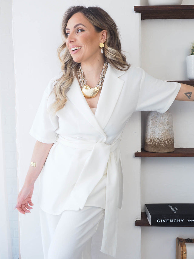 Mulher sorridente usando colar de búzios com pormenor de concha dourada, look elegante e boho.
