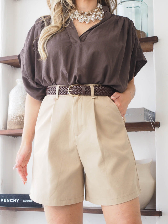 Cinto entrançado feminino com fivela dourada, combinando com blusa e shorts claros, estilo sofisticado e elegante.
