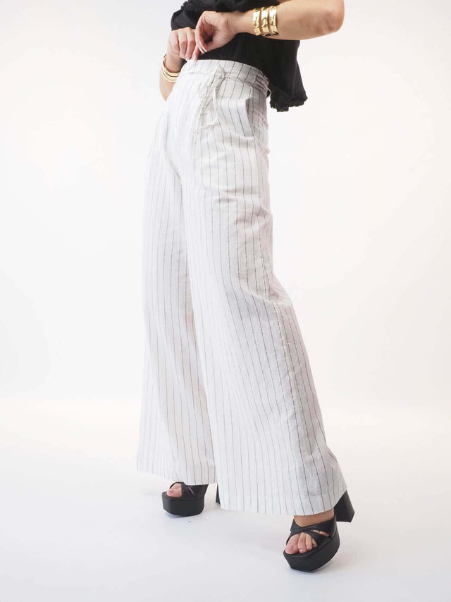 Calça clássica de senhora de corte largo, fundo branco com leve risca em preto com cintura alta, de bolsos e aperta de fecho e cinto.