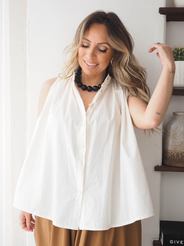 Mulher a sorrir com blusa branca e colar de pérolas grandes em resina, estilo elegante e contemporâneo.