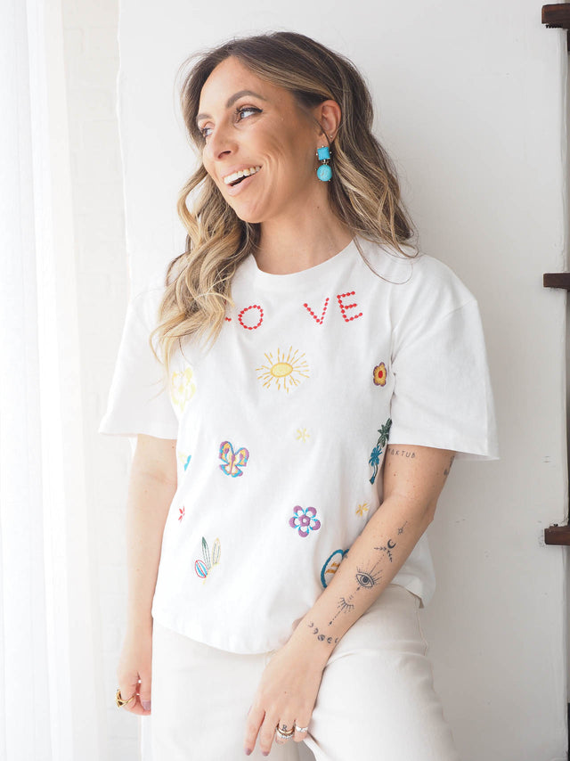 T-shirt de manga curta branca com bordados coloridos, ideal para looks casuais e confortáveis.