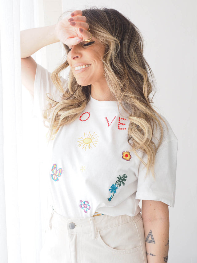 T-shirt branca com bordados coloridos e detalhes florais, perfeita para looks casuais e cheios de estilo.