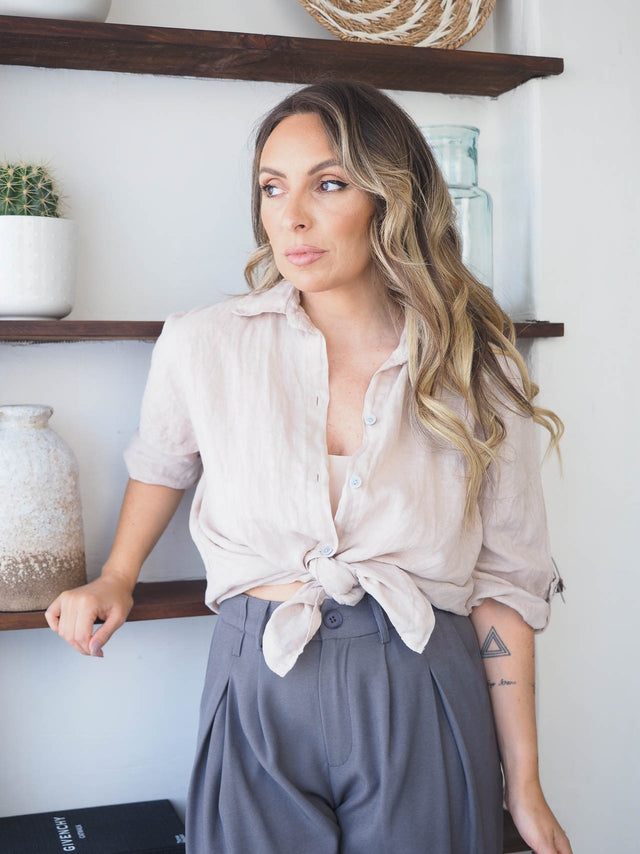 Mulher elegante usando uma camisa de linho clara com nó, combinada com calças elegantes em ambiente moderno.