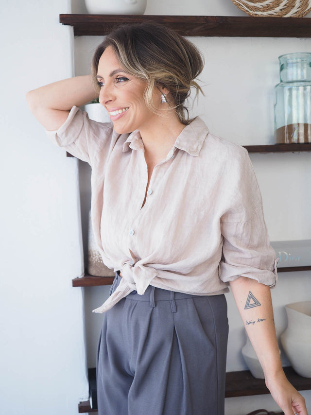 Mulher sorridente usando camisa de linho rosa claro, meia manga, estilo casual e elegante.