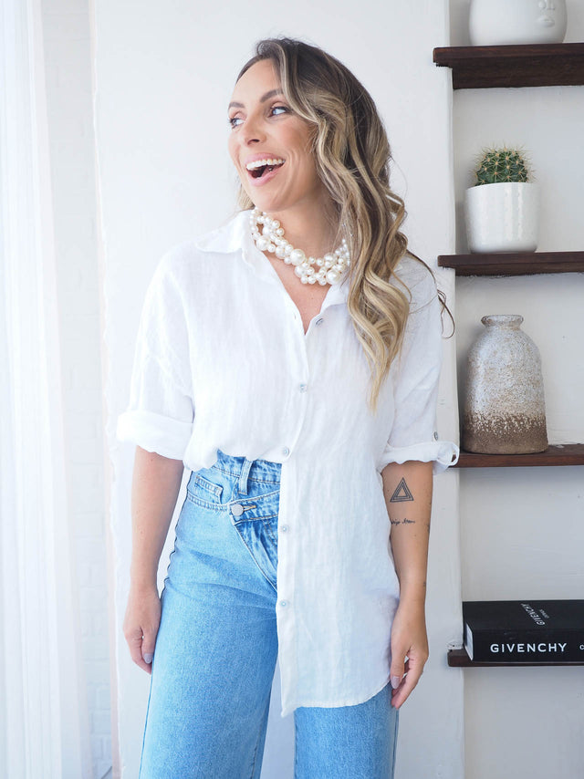 Mulher sorridente usando uma camisa de linho branca, perfeita para estilo e conforto em dias quentes.