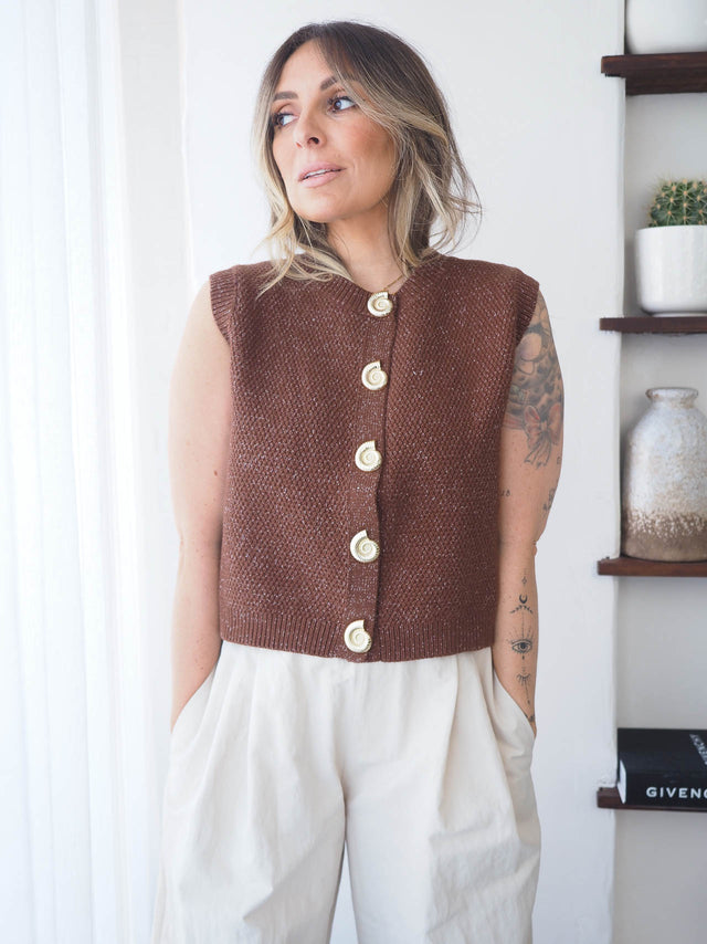 Colete de malha feminino em tom castanho, com botões e design sem mangas, combinação ideal para looks primavera-verão.