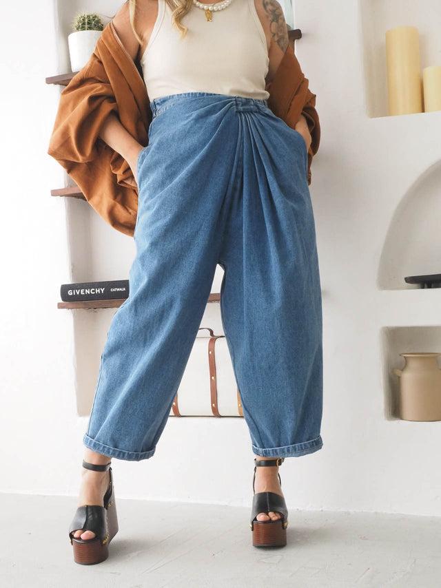 Calças baggy balloon em jeans, cintura alta, com detalhe de drapeado, combinadas com top e blazer feminino.