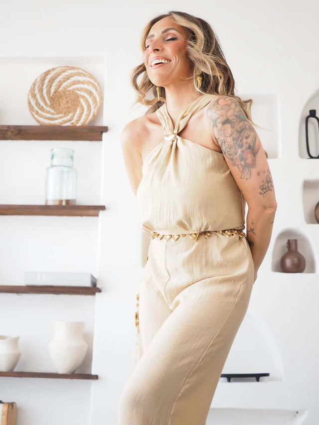 Macacão halter bege, plano de detalhe do decote e cinto dourado com argola.