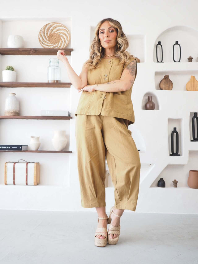 Conjunto colete e calças em linho mostarda, pose de braços cruzados, mostrando bolsos e botões.