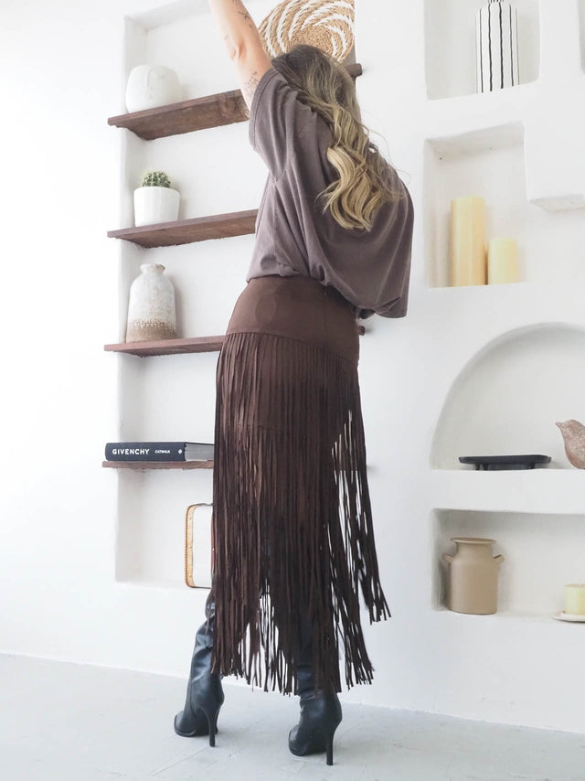 Saia com franjas em camurça castanha, perfeita para looks boho-chic, combinada com blusa oversized e botas altas.