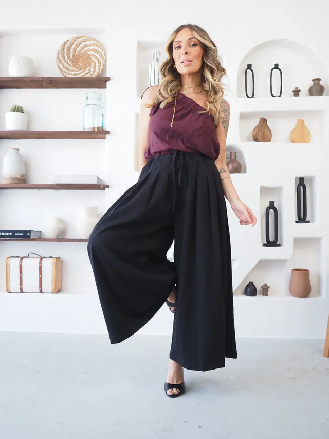 Mulher com blusa roxa e calças pantalona culote pretas largas.