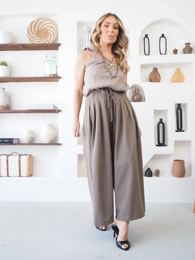 Mulher a usar calças pantalona culote em tom taupe, com corte largo.