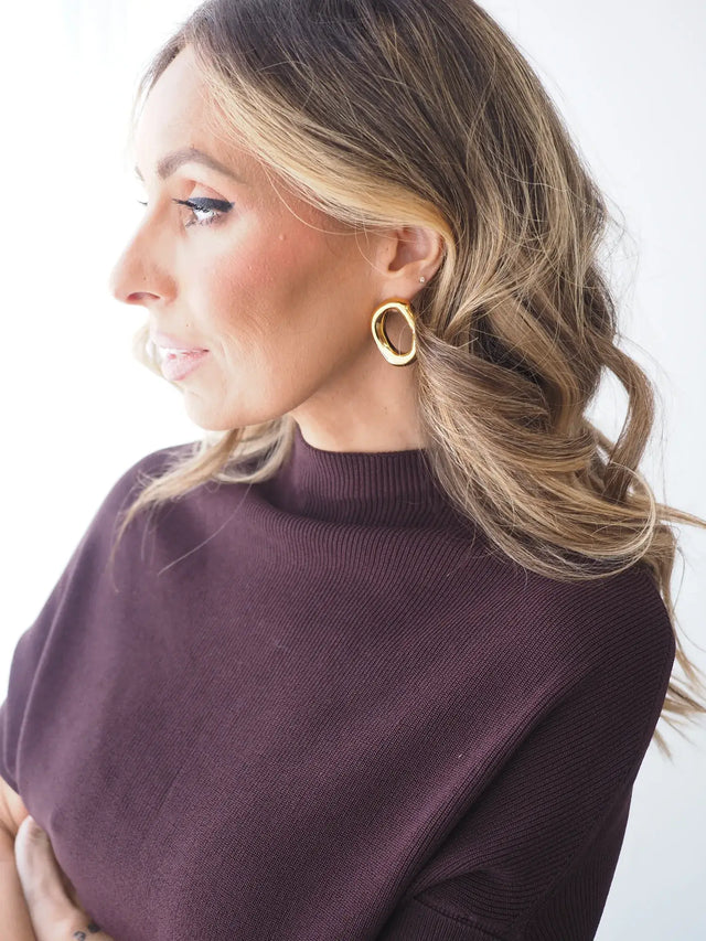 Mulher com brincos aros ovais em aço inoxidável e camisola roxa.