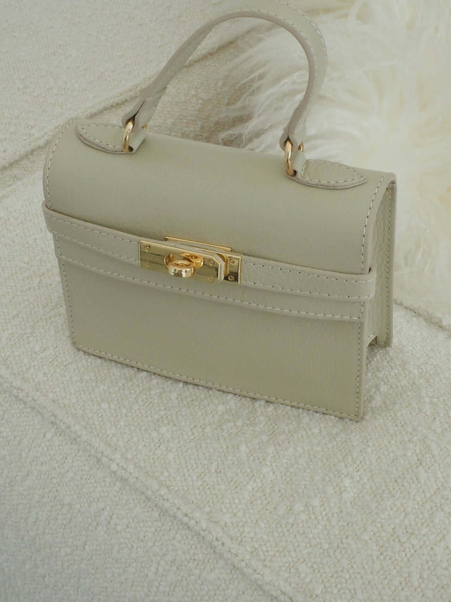 Mala com fecho de metal e pode ser usada com uma alça de mão ou de ombro (tira-colo).