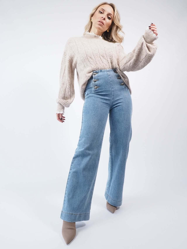 Conjunto de calças de ganga com uma camisola de malha bege.